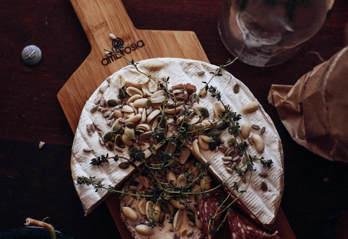 Camambert entamé, avec des cacahuètes et des herbes, servi sur une planche en bois.